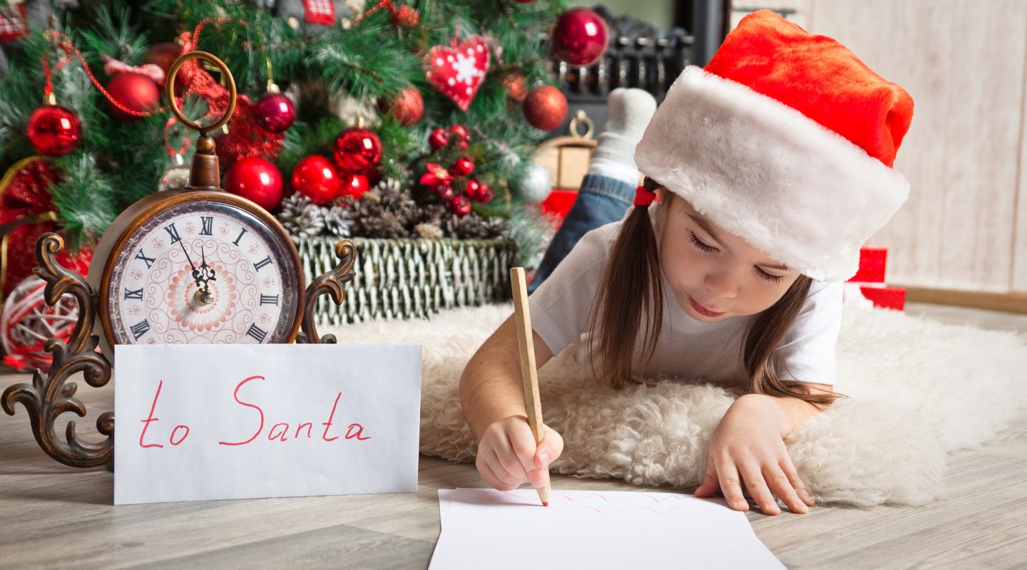 Pretty girl in Santa hat writes letter to Santa